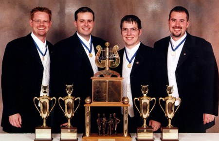 Four Voices, the 2002 International champions: four men in dark jackets with medals around their necks, their trophies in front.