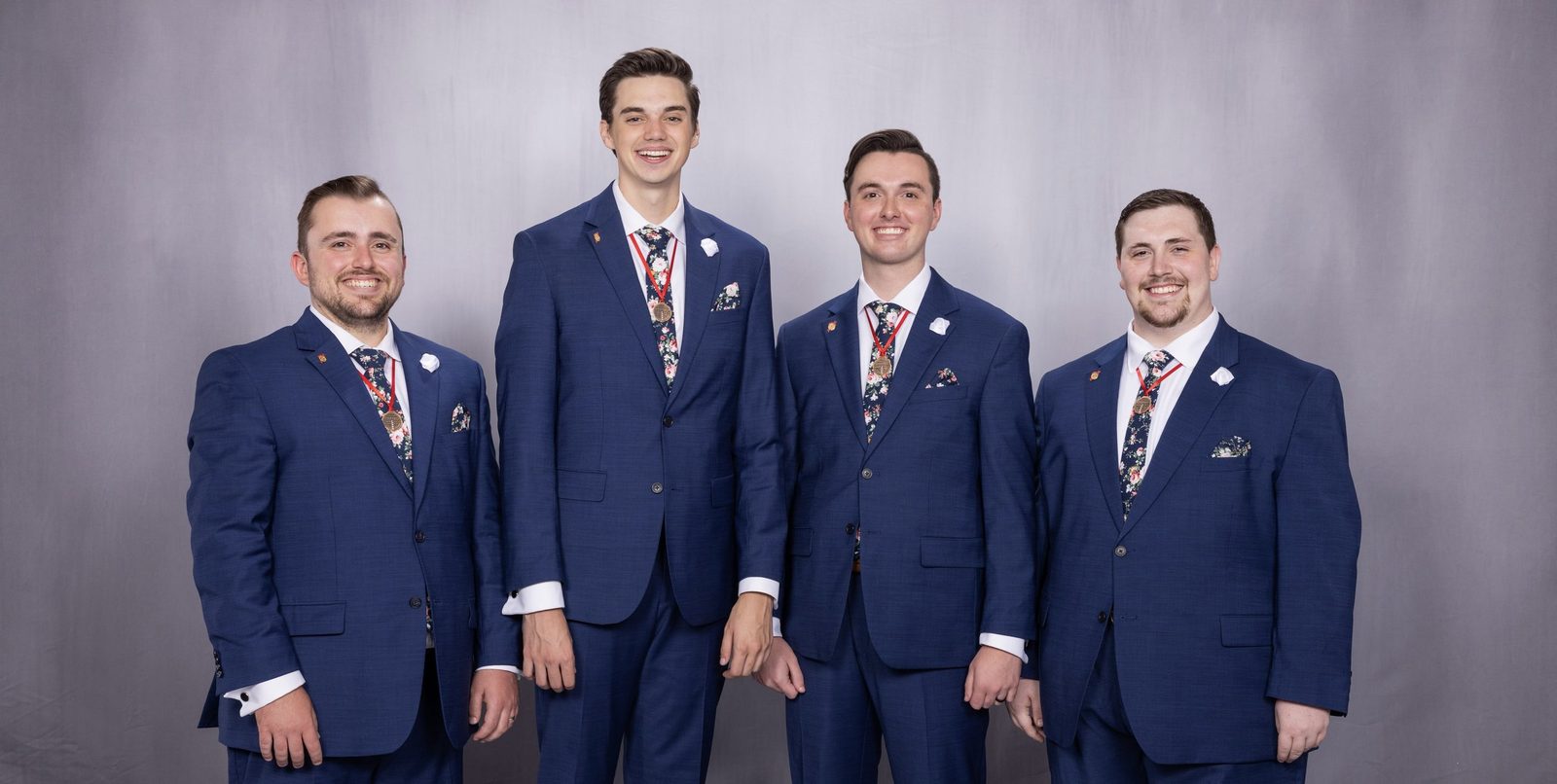 The four men of Full Effect in navy suits and floral ties, wearing their medals.