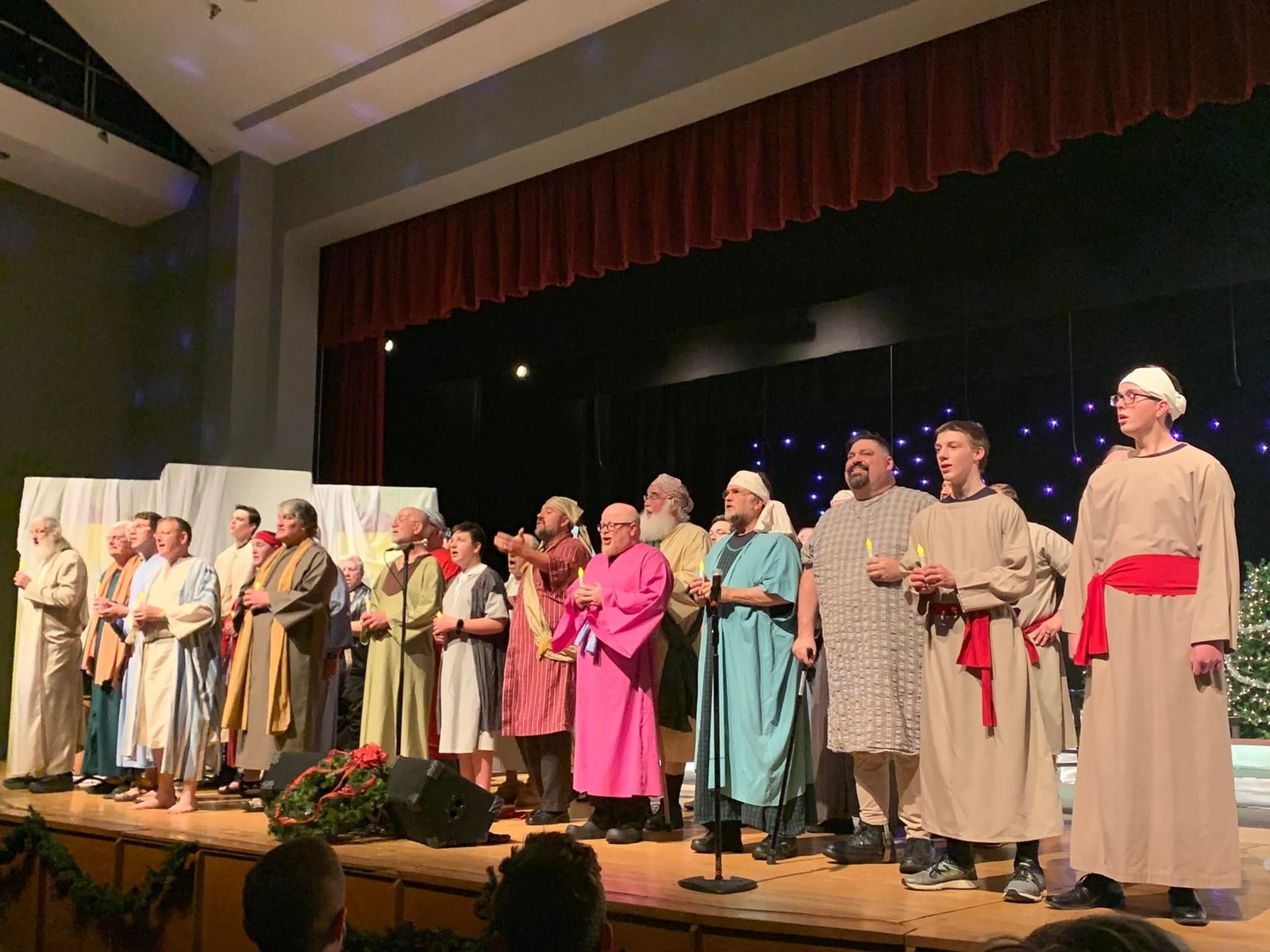 Chorus men in robes in a line across a stage, some holding candles, at the 2021 Christmas show.