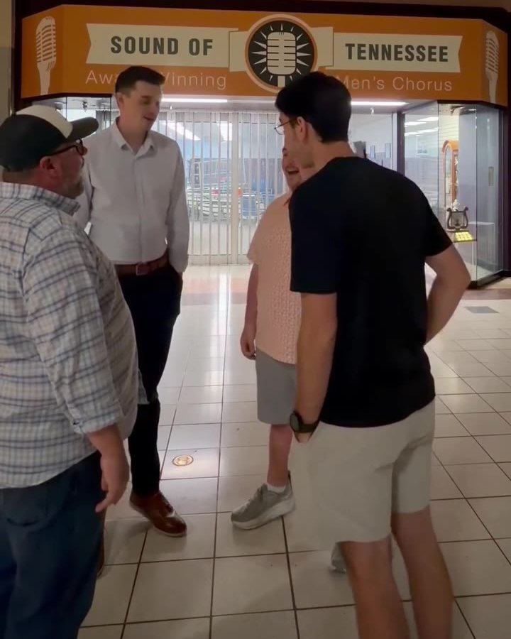 Four men in a loose circle singing in a mall corridor, the orange Sound of Tennessee storefront sign behind them.