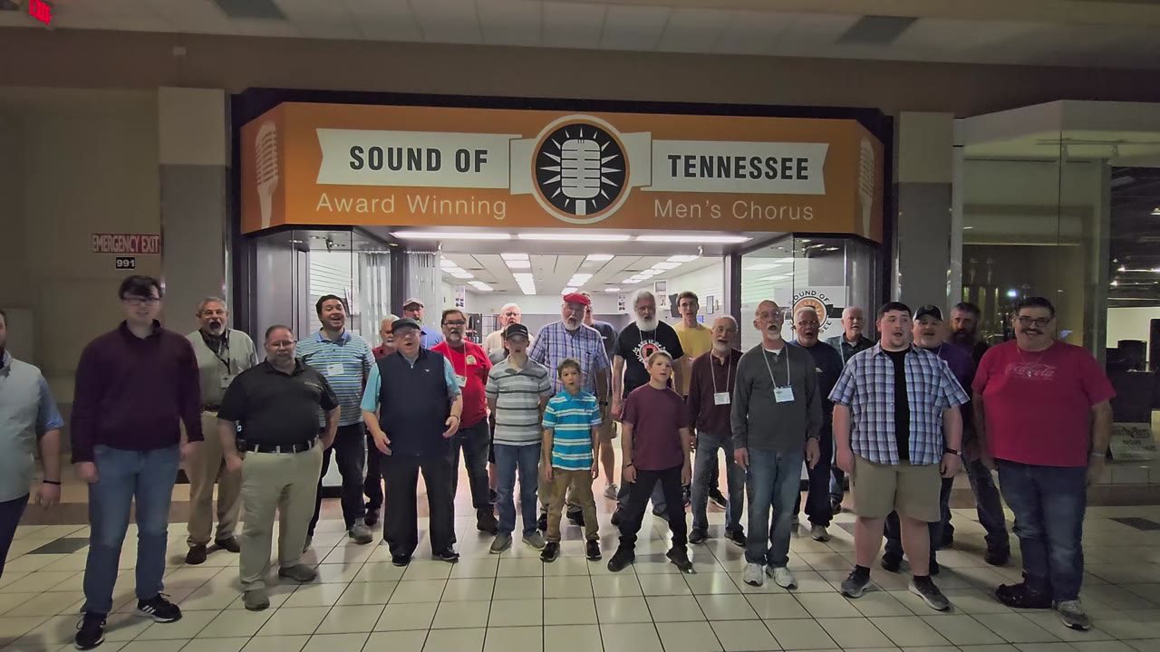 About forty men singing in a mall corridor in front of the orange Sound of Tennessee sign.